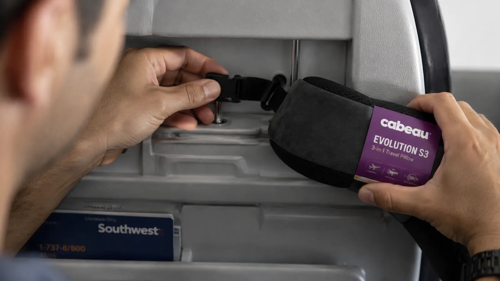 Hand adjusting the seat strap clip of the Cabeau Evolution S3 neck pillow on an airplane headrest